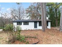 Charming single-story home with a white brick exterior and black framed windows, nestled among mature trees at 3215 Pennignton Cir, Atlanta, GA 30354