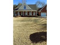Charming brick home with a welcoming front porch, two-car garage and a large yard on a sunny day at 216 Brackin Trce, Grayson, GA 30017
