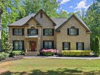 Charming two-story brick home with a well-manicured lawn, mature trees, and a welcoming red front door at 4680 Brighton Lake Dr, Cumming, GA 30040