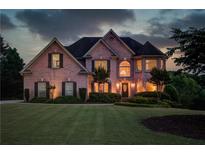 Elegant brick home featuring manicured lawn, lush landscaping and warm, inviting exterior lighting at 1608 Mulberry Lake Dr, Dacula, GA 30019