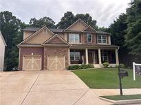 Charming two-story home with a combination of brick and stone accents, a well-manicured lawn, and a welcoming front porch at 6725 Grove Meadows Ln, Cumming, GA 30028