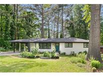 Charming white brick home featuring a bright teal front door, lush lawn, and mature trees at 2425 Clifton Springs Rd, Decatur, GA 30034