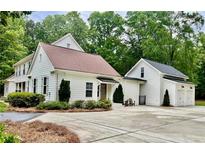 Charming white home with a spacious driveway and a detached garage, surrounded by lush greenery and mature trees at 400 N Peachtree Pkwy, Peachtree City, GA 30269