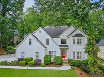 Charming two-story home with a red front door and lush landscaping in a serene, wooded setting at 10000 Groomsbridge Rd, Johns Creek, GA 30022