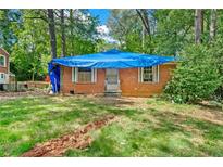View of a brick home with a blue tarp covering the roof and an overgrown front yard at 2180 Rexford Dr, Decatur, GA 30034