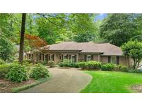 Charming one story brick home featuring a circular driveway and lush landscaping with mature trees at 11190 Hembree Springs Dr, Roswell, GA 30076