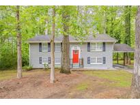Charming two-story home with grey brick, black shutters, red door, and a covered parking area surrounded by lush trees at 3084 Fern Valley Sw Dr, Marietta, GA 30008