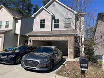 Two-story home with gray siding, brick accents, attached garage, and two cars parked in the driveway at 2347 Hackamore Dr, Atlanta, GA 30349