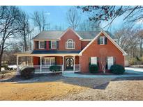 Charming two-story red brick home with a covered front porch and well-manicured landscaping on a sunny day at 2995 Aspen Ridge Ct, Snellville, GA 30078