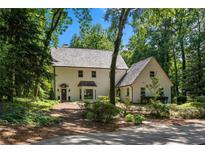 Charming two-story home with a neutral color palette, nestled amongst mature trees and lush landscaping on a sunny day at 1260 Heards Ferry Rd, Sandy Springs, GA 30328