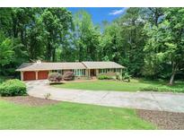 Charming home boasts a lush, green lawn and a circular driveway surrounded by mature trees at 5170 Oxbow Rd, Stone Mountain, GA 30087
