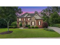 Charming two-story brick home with stone accents, well-manicured lawn, and mature trees during sunset at 5925 Water Mark Dr, Cumming, GA 30040