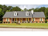 Charming brick home featuring a manicured lawn, dormer windows, and a welcoming front porch with yellow accents at 40 Oak Hill Dr, Covington, GA 30016