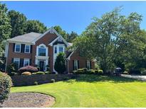 Imposing brick home featuring a manicured lawn, mature trees, and distinguished architectural details at 10830 Carrara Cv, Alpharetta, GA 30022