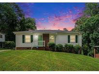 Charming single-story home featuring white siding, brick accents, green shutters and a lush front lawn against a colorful sunset at 3650 Croft Nw Pl, Atlanta, GA 30331