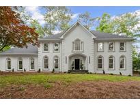 Elegant white home featuring symmetrical design, arched windows, and professionally landscaped front yard at 605 Buttercup Trce, Johns Creek, GA 30022
