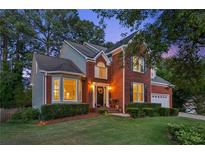 Charming brick home featuring manicured lawn, mature trees and inviting front entrance at twilight at 440 Laurian Nw Way, Kennesaw, GA 30144