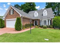 Charming brick home with lush lawn, mature trees, and a brick driveway leading to a two-car garage at 567 N Palisades Se Cir, Marietta, GA 30067