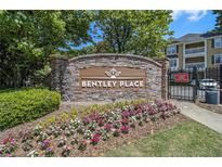 Stone sign for Bentley Place with colorful flowers and a glimpse of the buildings behind the gated entrance at 328 Bentley Pl # 328, Tucker, GA 30084