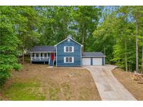 Charming two-story blue home featuring a welcoming front porch and an attached two-car garage, nestled among lush trees at 5200 Beechwood Forest Ct, Lithonia, GA 30038