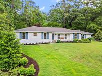 Charming one-story home with white brick, blue shutters, and a lush green lawn surrounded by mature trees at 4855 Kendall Ct, Atlanta, GA 30342
