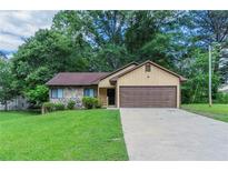 Charming single-story home with a stone accent wall, a brown garage door, and a lush green lawn at 8350 Gledstone Way, Fairburn, GA 30213