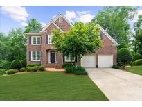 Charming brick home with a manicured lawn, two-car garage, and lush landscaping at 7049 Bennington Ln, Cumming, GA 30041