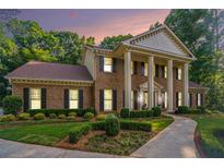 Charming brick home featuring a columned entryway, manicured lawn, and lush landscaping at 2080 Old Dominion Rd, Atlanta, GA 30350