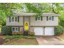 Charming home features a bright yellow door, a two-car garage, and lovely landscaping at 4171 Whispering Forest Sw Ct, Lilburn, GA 30047