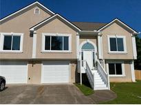 Beige two-story home with a two-car garage, white trim, and a staircase leading to the front door at 102 Peaceful Vw, Acworth, GA 30102