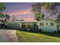 Charming white brick home featuring a covered front porch, attached garage and lush green lawn at 4384 Herschel Rd, College Park, GA 30337