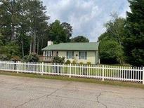 Charming single-story home with a green roof and a white picket fence bordering a manicured front yard at 173 Elder Dr, Social Circle, GA 30025