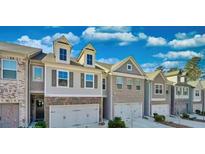 Attractive townhome exterior with a well-maintained lawn and attached garages underneath a partly cloudy, blue sky at 2711 Kemp Ct, Conyers, GA 30094