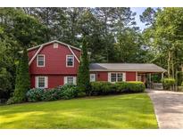 Charming red two-story home with a well-manicured lawn, lush landscaping, and a driveway leading to the carport at 1102 Waverly Dr, Lawrenceville, GA 30046