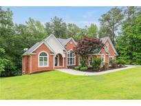 Charming red brick home featuring an immaculate lawn, arched windows, and professional landscaping at 7406 Cherry Blossom Way, Winston, GA 30187