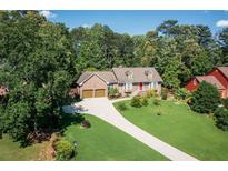 Charming brick home with a lush green lawn, mature trees, and a long driveway leading to a two-car garage at 2702 Moorings Pkwy, Snellville, GA 30039