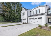 A view of a modern white townhouse with attached garage, complemented by a concrete driveway and manicured landscaping at 1704 Hyssop Se Blvd, Smyrna, GA 30126