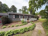 Charming single-story home featuring a gray brick facade, white trim, a quaint front porch, and mature landscaping at 2857 Spanish Oak Sw Dr, Lilburn, GA 30047