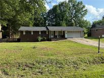 Brick house with an attached garage and driveway is surrounded by mature trees and an unkempt lawn at 1024 Topaz Lane, Villa Rica, GA 30180