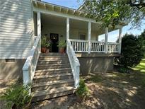 Inviting front porch with white railing, staircase and potted plants adds charm to this home's exterior at 2 N Broad St, Porterdale, GA 30070