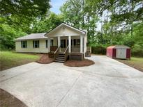 Charming home with front porch and a concrete driveway surrounded by green trees and a storage shed in the back at 355 Marietta Hwy, Roswell, GA 30075