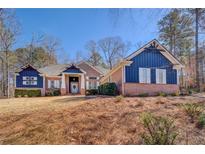 Inviting exterior of a brick and blue home with dormers, front yard, and mature trees under a sunny blue sky at 410 Fitzgerald Ln, Fayetteville, GA 30215