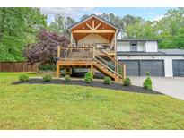 Charming home exterior featuring a wood deck, landscaped yard, and attached two-car garage at 110 W Putnam Ferry Rd, Woodstock, GA 30189