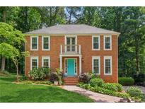 Charming two-story brick home featuring a bright blue front door, well-manicured lawn, and lush landscaping at 2696 Chancellor Way, Duluth, GA 30096