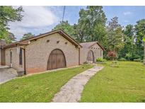 Charming brick home featuring unique arched doorways and mature landscaping on a sprawling green lawn at 4296 Linda Sw Ln, Lilburn, GA 30047