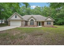 Charming brick home featuring an attached two-car garage, green lawn, and mature trees at 25 Pebble Creek Dr, Covington, GA 30016