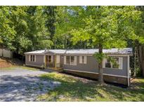 Charming gray home with a metal roof, complemented by lush, mature trees and a gravel driveway at 6235 Akins Way, Cumming, GA 30041