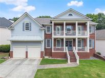 Charming two-story home featuring a covered front porch with columns, gray siding, brick accents, and a well-manicured lawn at 2100 Willshire Gln, Alpharetta, GA 30009