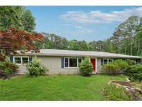 Charming one-story home featuring a manicured lawn, mature trees, and a welcoming red front door at 1926 Parkwood Rd, Snellville, GA 30078