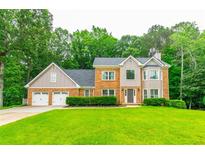 Charming two-story brick home featuring a three-car garage and a well-manicured lawn with mature trees at 3394 Floral Ct, Suwanee, GA 30024